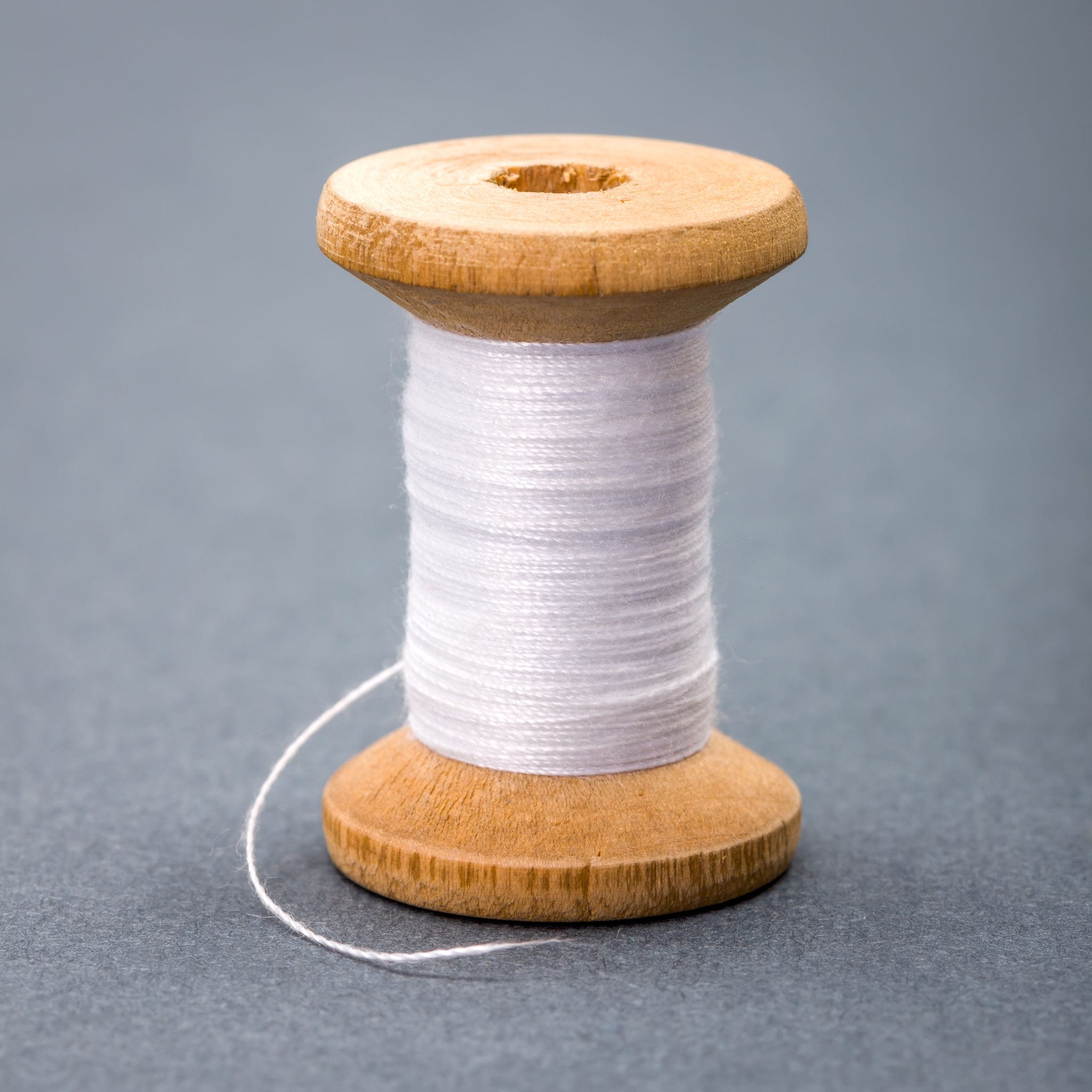 Vintage wooden spool of white sewing thread Vintage wooden spool of white sewing thread on gray background